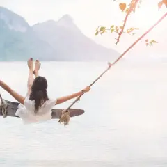 En kvinna gungar över lugnt vatten, en bild av frid och välbefinnande, som påminner om ayurveda yoga.