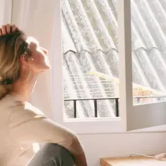 En kvinna sitter vid ett fönster, med handen i håret, och blickar uppåt. Ljuset faller på henne, men hon verkar drabbad av årstidsbunden depression.