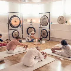 Grupp utför medicinsk yoga på stol i ett rum med gongs.