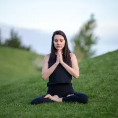 Kvinna i lotusställning på en grön kulle, som en yoga blomma i naturen.