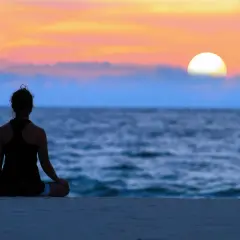 En person sitter i lotusställning på en strand vid solnedgången. En stund av mindfulness i vardagen.