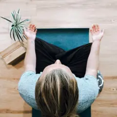 Person mediterar på en matta, kanske funderar på nackdelar med meditation. En växt och träklossar syns bredvid.