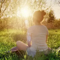 En person sitter i gräset i solnedgången, en lugn typ av meditation.
