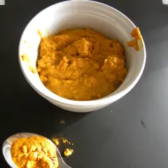 En skål med gyllene gurkmeja pasta bredvid en sked full av pulveriserad gurkmeja.