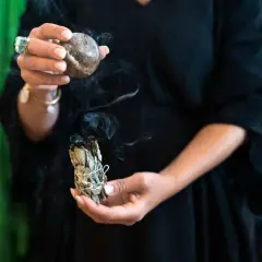 En person håller en rökande salviabunt och en sten. Rena kristaller kan ge energi till ritualen.