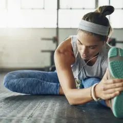 Kvinna stretchar benet på gymgolvet, lyssnar på musik. En del av hennes fascia yoga-rutin.