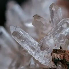Klar kvarts sten med spetsiga kristaller som växer ur en brunaktig bas.