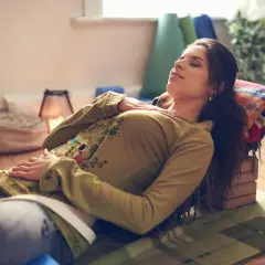 Kvinna vilar med slutna ögon, upplever lugnande yoga nidra effekter. Stöd för huvud och kropp, omgiven av yogatillbehör.