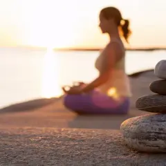 En kvinna mediterar vid solnedgången, en stenhög som ett mantra exempel på lugn.