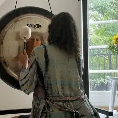 Person i färgglad kimono förbereder sig för gong bad. En stor gong står framför ett fönster med solrosor.