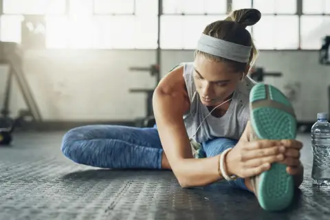 Kvinna stretchar benet på gymgolvet, lyssnar på musik. En del av hennes fascia yoga-rutin.