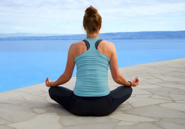 Jenny hittar lugnet med jennys mindfulness vid en infinitypool med utsikt över ett blått hav och berg.