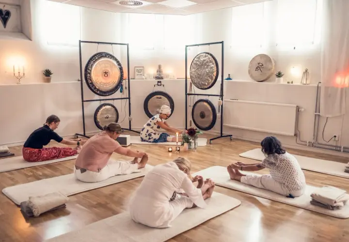 Grupp utför medicinsk yoga på stol i ett rum med gongs.