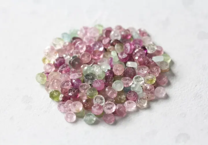 En hög med små, fasetterade turmaliner i olika färger, från rosa till grönt. Dessa stenar sägs ha helande turmalin egenskaper.