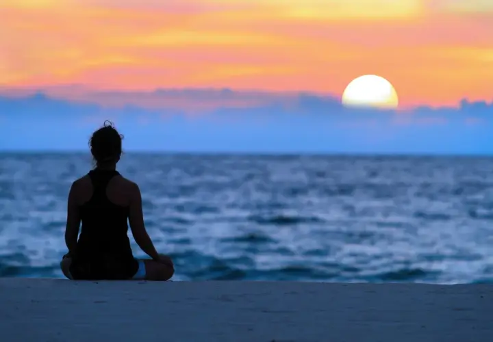 En person sitter i lotusställning på en strand vid solnedgången. En stund av mindfulness i vardagen.