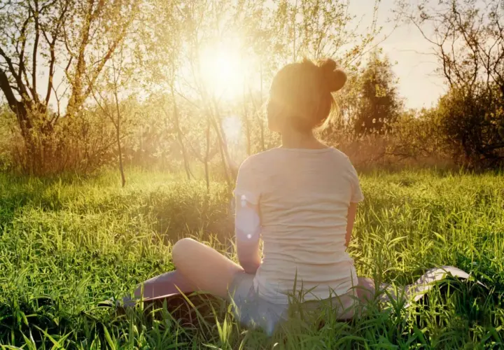 En person sitter i gräset i solnedgången, en lugn typ av meditation.