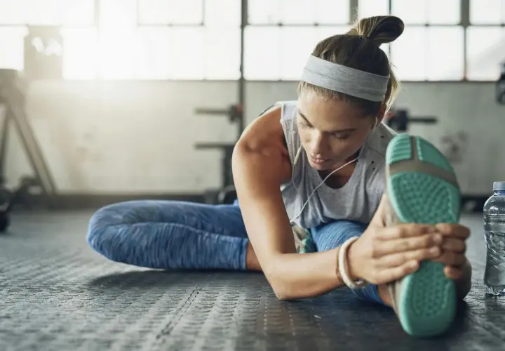 Kvinna stretchar benet på gymgolvet, lyssnar på musik. En del av hennes fascia yoga-rutin.