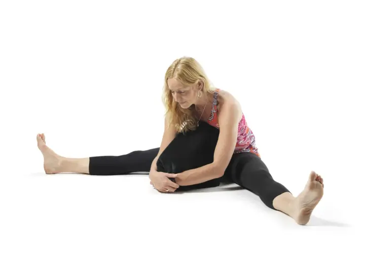Kvinna i yin yoga-position med benen isär och en kudde mot bröstet. Utforska yin yoga effekter för ökad rörlighet och lugn.