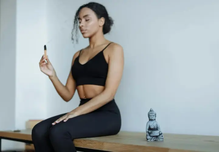 Kvinna med slutna ögon håller en rökelsepinne, en Buddha-statyett bredvid. Forskning om sa ta na ma meditation.