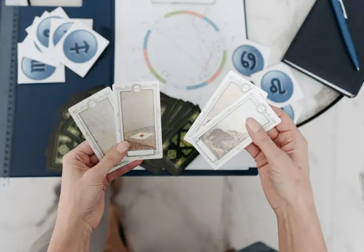 Händer håller tarotkort med symboler för sjunde huset astrologi. En astrologisk karta och stjärntecken syns i bakgrunden.