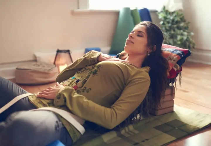 Kvinna vilar med slutna ögon, upplever lugnande yoga nidra effekter. Stöd för huvud och kropp, omgiven av yogatillbehör.