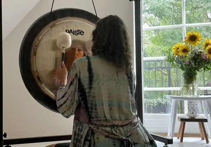 Person i färgglad kimono förbereder sig för gong bad. En stor gong står framför ett fönster med solrosor.