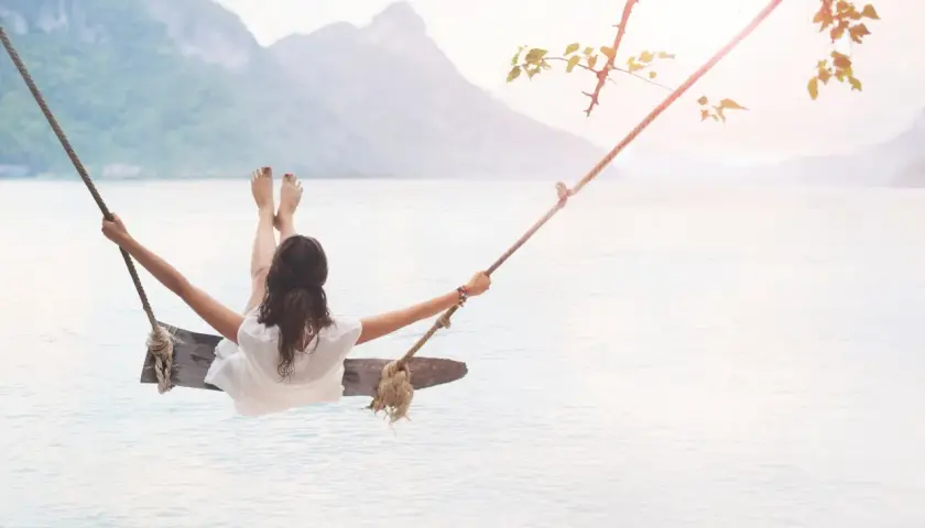 En kvinna gungar över lugnt vatten, en bild av frid och välbefinnande, som påminner om ayurveda yoga.