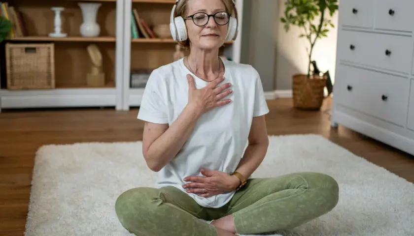 Kvinna med hörlurar sitter på en matta och fokuserar på sin andning för att slappna av.