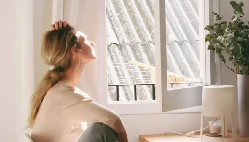 En kvinna sitter vid ett fönster, med handen i håret, och blickar uppåt. Ljuset faller på henne, men hon verkar drabbad av årstidsbunden depression.