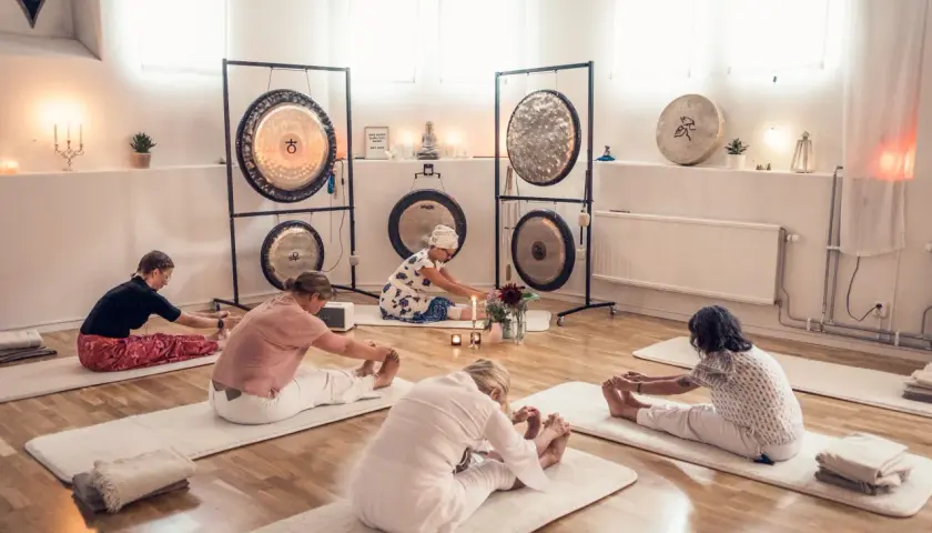 Grupp utför medicinsk yoga på stol i ett rum med gongs.