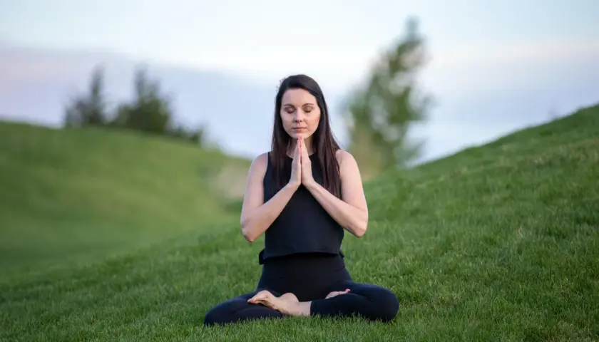 Kvinna i lotusställning på en grön kulle, som en yoga blomma i naturen.