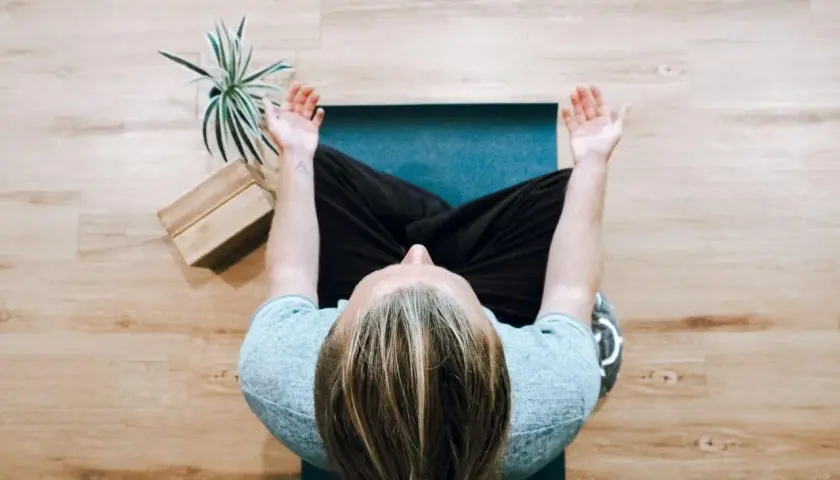 Person mediterar på en matta, kanske funderar på nackdelar med meditation. En växt och träklossar syns bredvid.