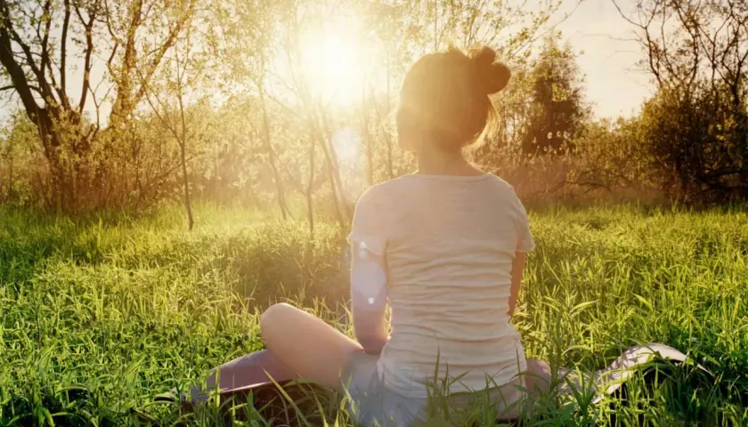En person sitter i gräset i solnedgången, en lugn typ av meditation.