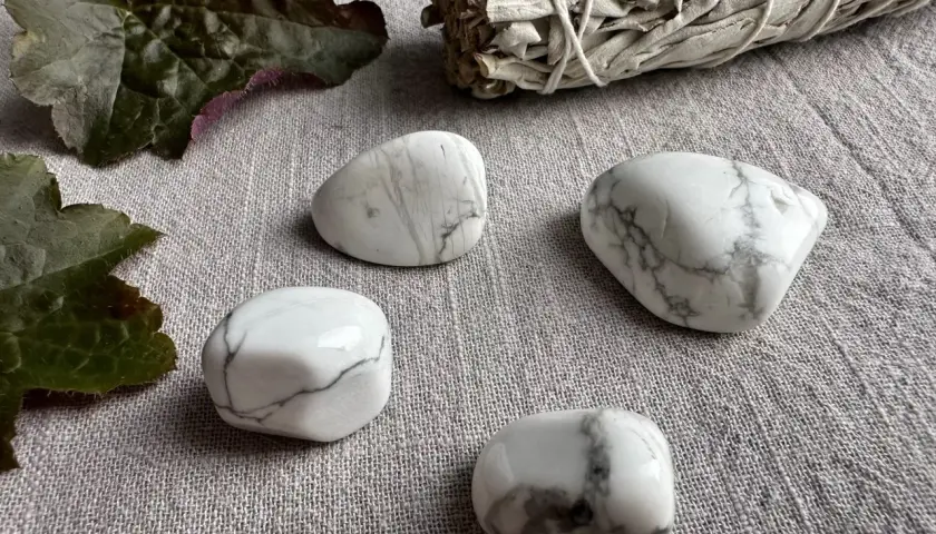 Fyra vita stenar med grå ådring, troligen magnesit, ligger på en grå duk. En bunt salvia och mörka blad ligger bredvid. Magnesit egenskaper kan vara lugnande.