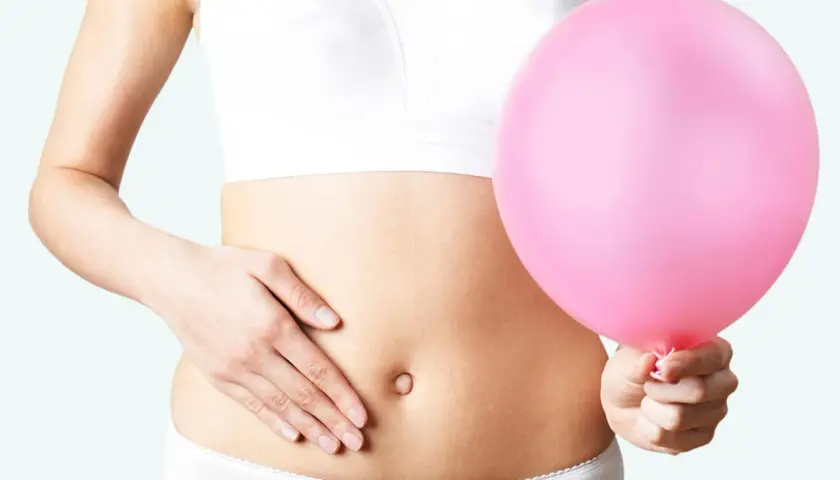 Kvinna håller en rosa ballong vid magen, en visuell representation av husmorstips för svullen mage.