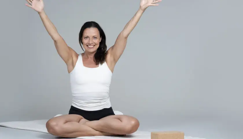 Kvinna i meditationsställning med armarna uppåt, utstrålar lugn och glädje. Hon praktiserar metta meditation för inre frid.
