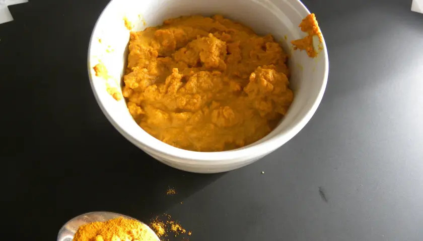 En skål med gyllene gurkmeja pasta bredvid en sked full av pulveriserad gurkmeja.