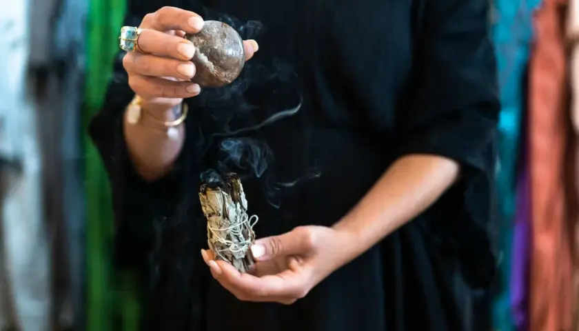 En person håller en rökande salviabunt och en sten. Rena kristaller kan ge energi till ritualen.