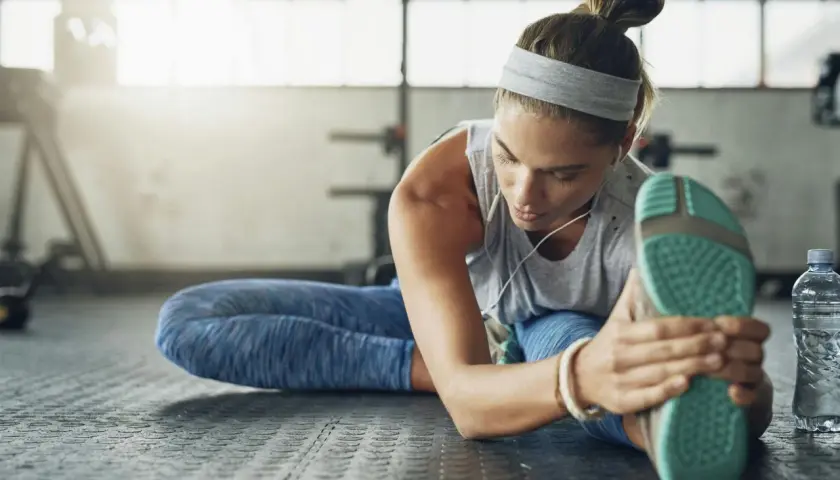 Kvinna stretchar benet på gymgolvet, lyssnar på musik. En del av hennes fascia yoga-rutin.