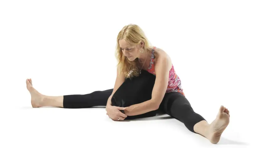 Kvinna i yin yoga-position med benen isär och en kudde mot bröstet. Utforska yin yoga effekter för ökad rörlighet och lugn.