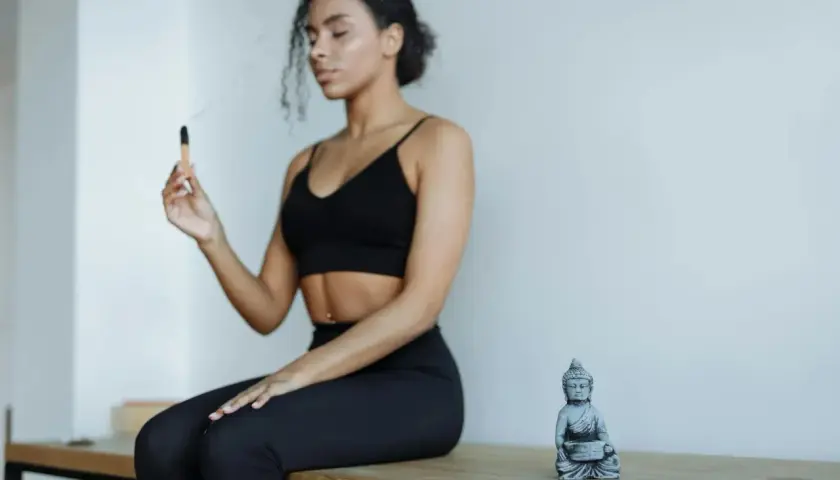 Kvinna med slutna ögon håller en rökelsepinne, en Buddha-statyett bredvid. Forskning om sa ta na ma meditation.