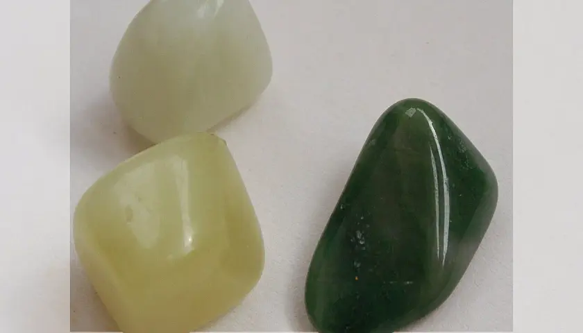 Three smooth, polished jade stones: one pale green, one light yellow-green, and one dark green.