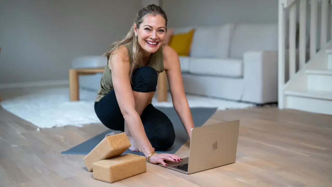 Glad kvinna förbereder sig för en lugn yogaövning med hjälp av en laptop och **restorative yoga positioner**.