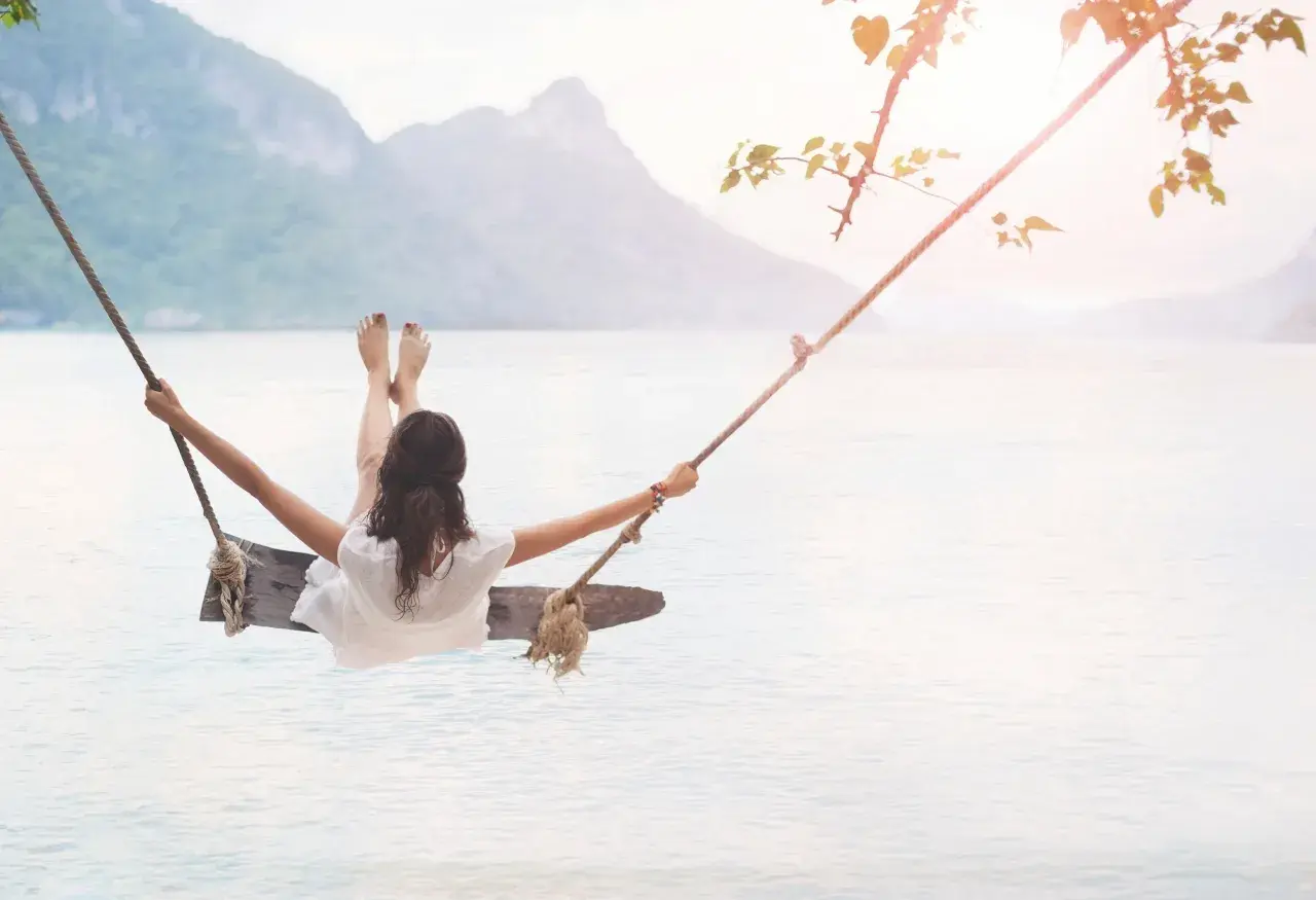 En kvinna gungar över lugnt vatten, en bild av frid och välbefinnande, som påminner om ayurveda yoga.