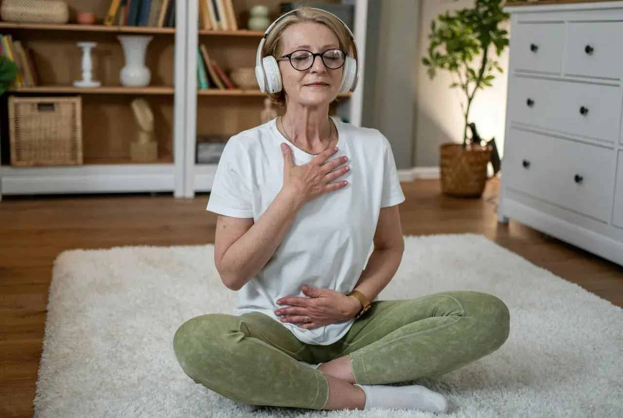 Kvinna med hörlurar sitter på en matta och fokuserar på sin andning för att slappna av.