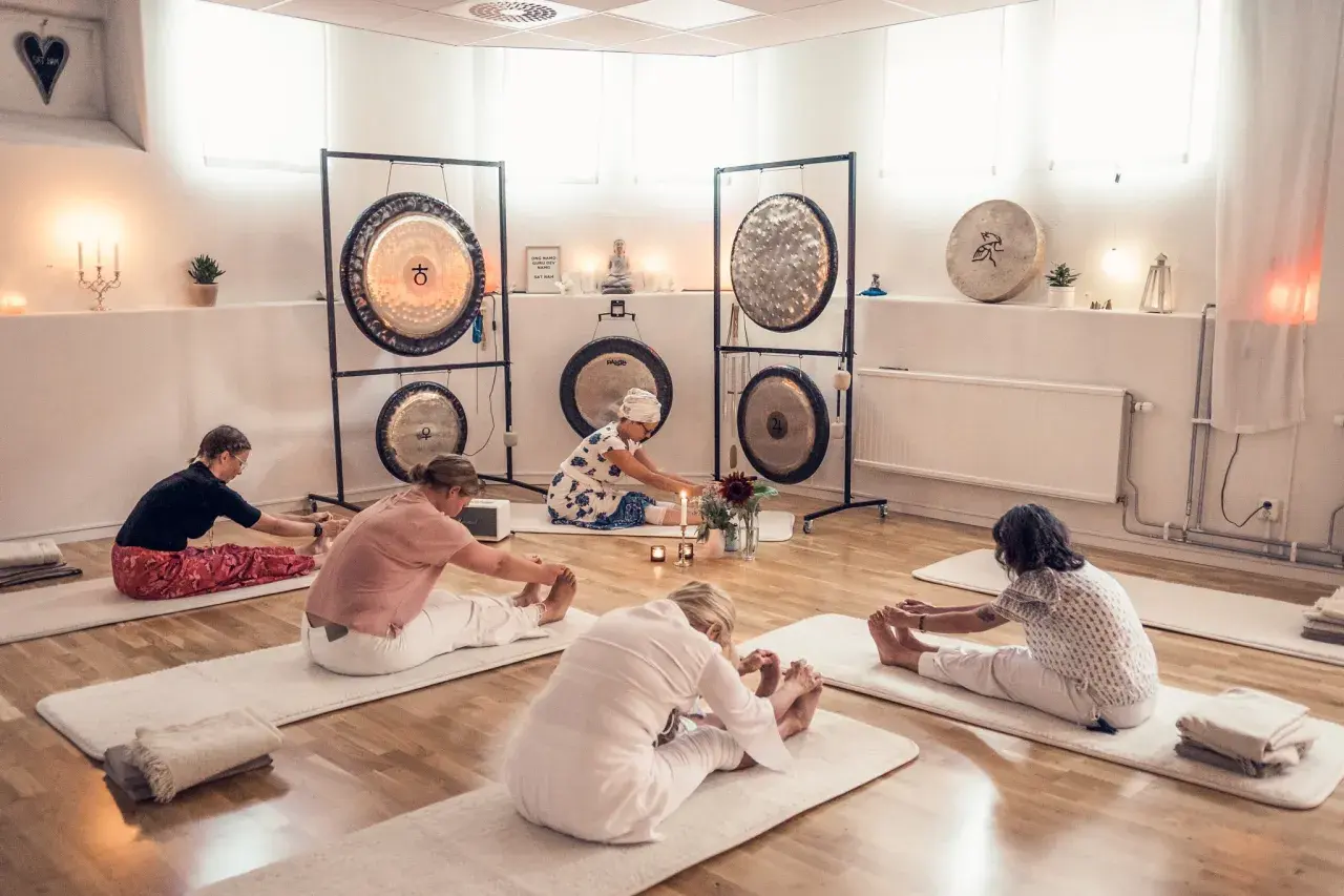 Grupp utför medicinsk yoga på stol i ett rum med gongs.