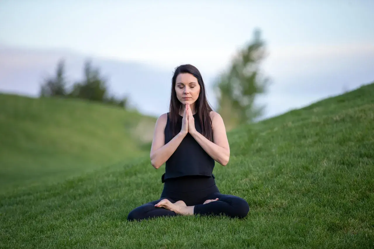 Kvinna i lotusställning på en grön kulle, som en yoga blomma i naturen.