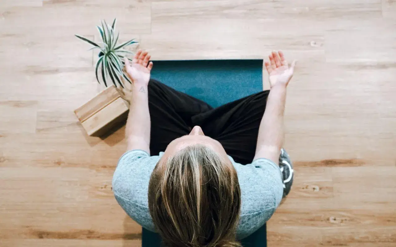 Person mediterar på en matta, kanske funderar på nackdelar med meditation. En växt och träklossar syns bredvid.