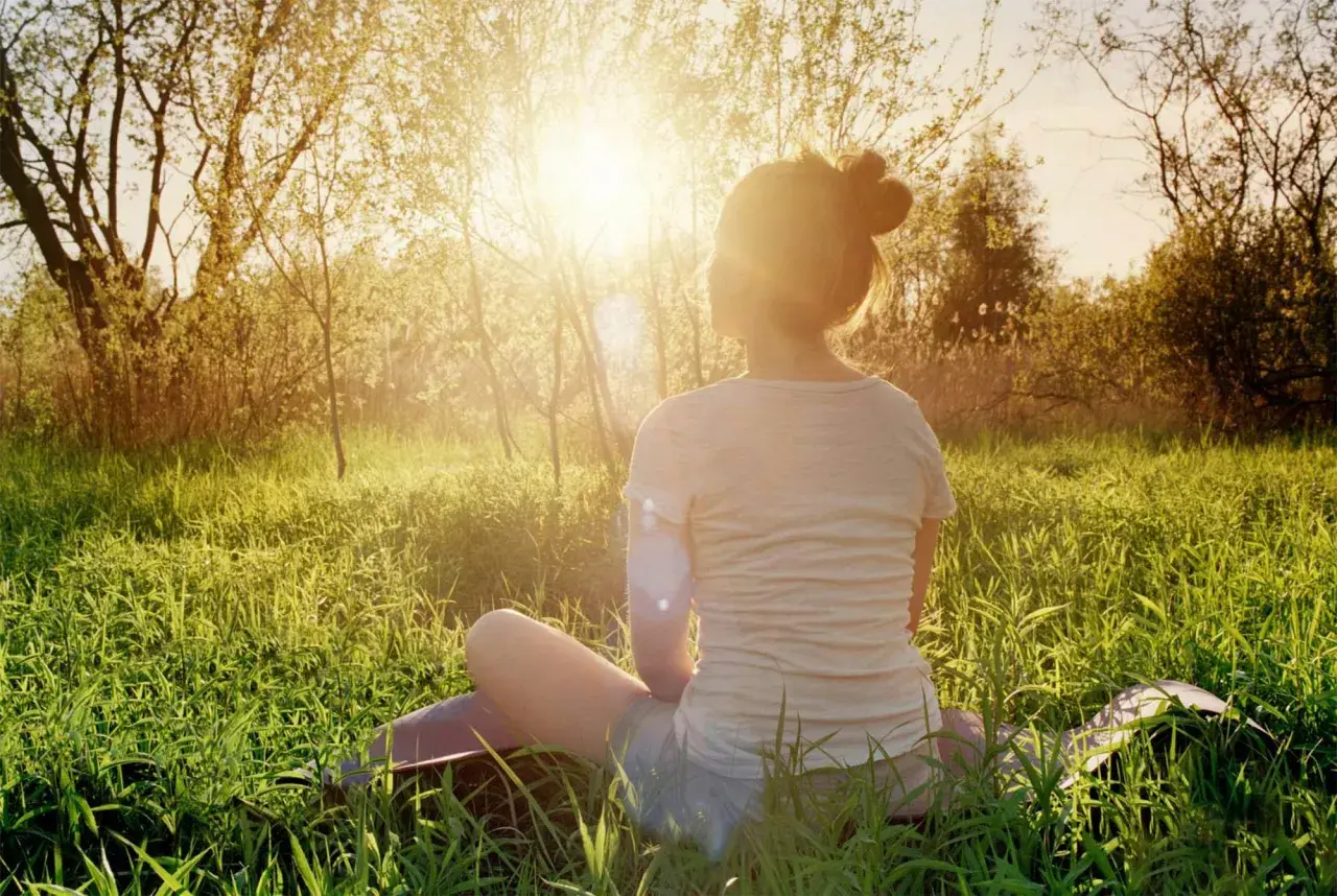 En person sitter i gräset i solnedgången, en lugn typ av meditation.