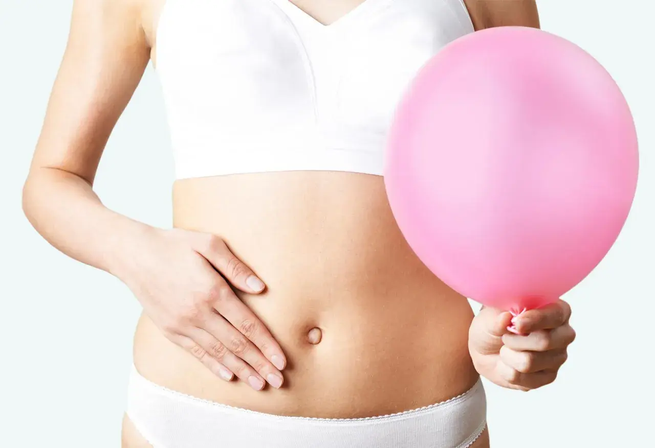 Kvinna håller en rosa ballong vid magen, en visuell representation av husmorstips för svullen mage.